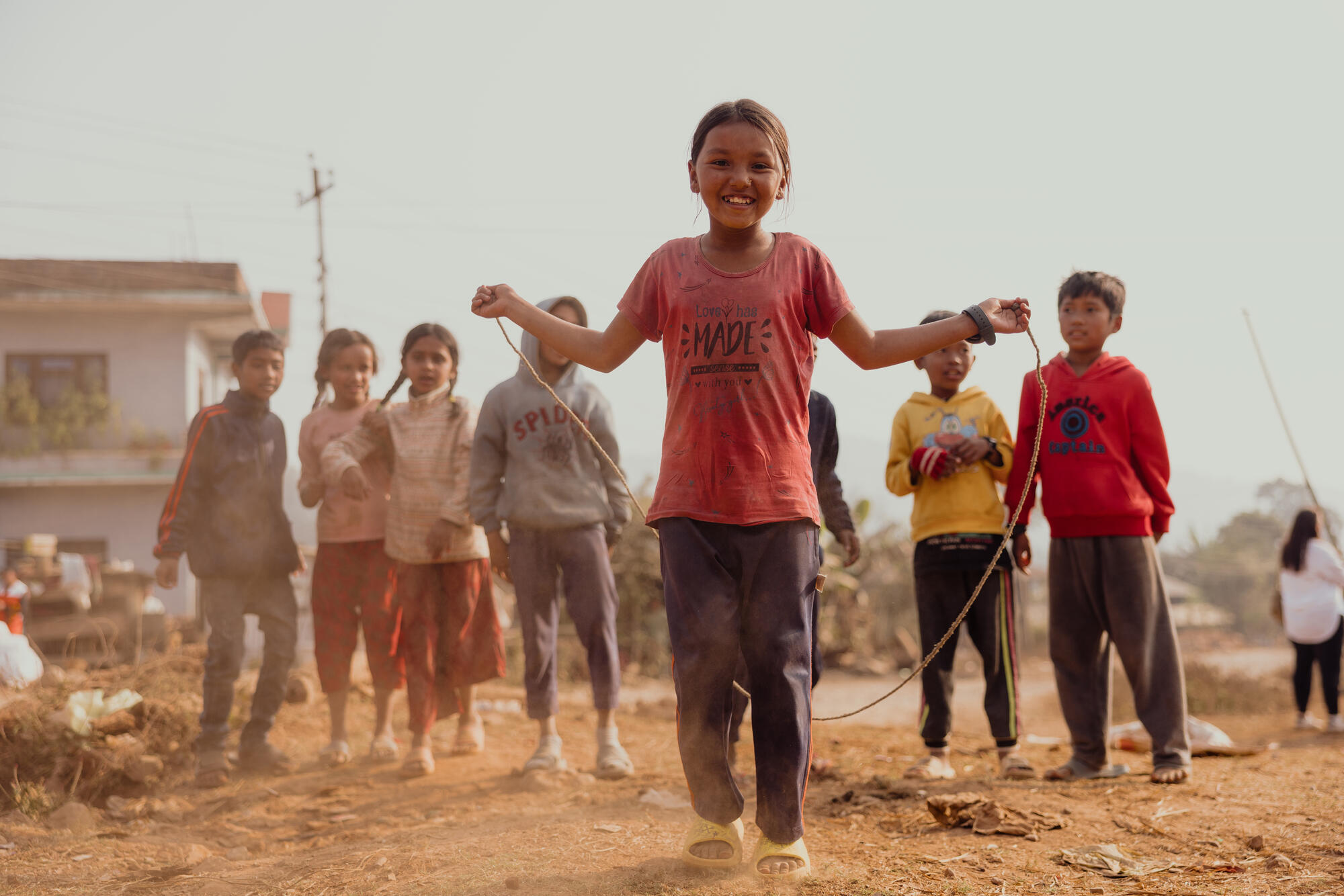 A child in Nepal jumps over a skipping rope with other children playing in the background