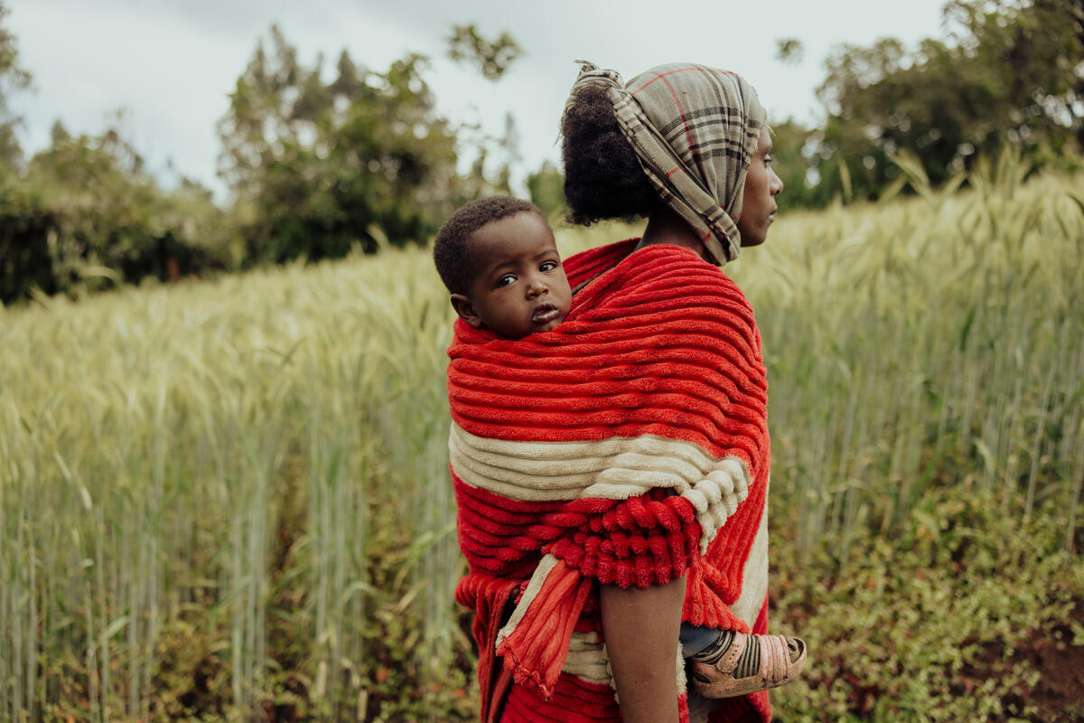 Young Ethiopian girl carries a baby on her back, she's walking in a field