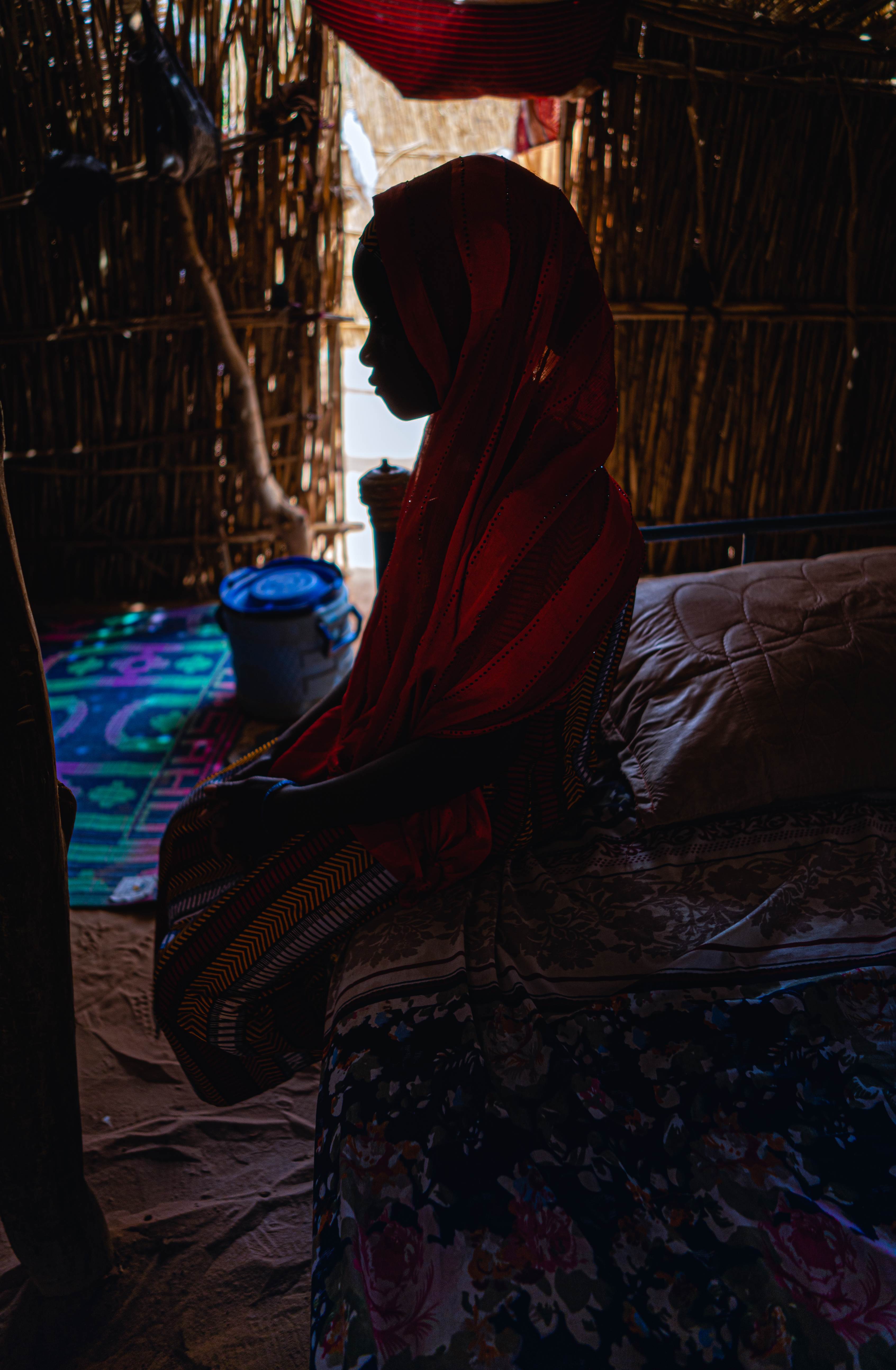 Girl from Niger sits, face in shadow, in a room, looking down