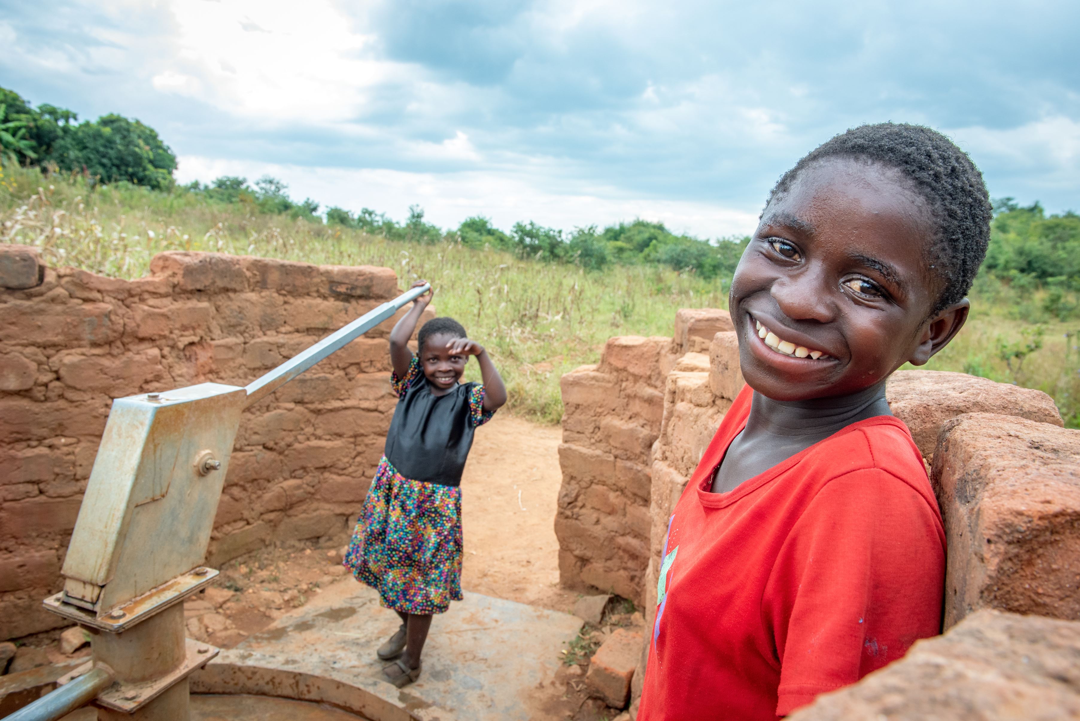 Girl in a red t-shirt smiles to camera at a borehole