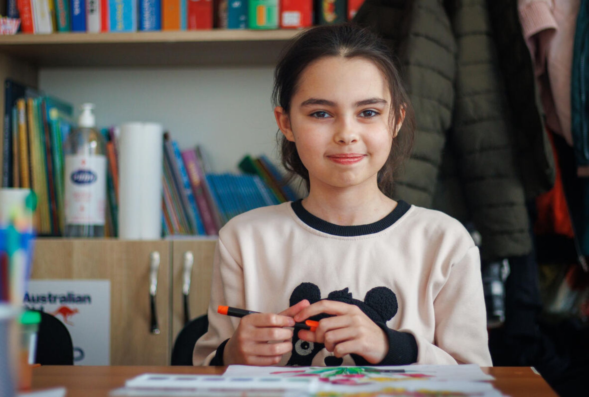 Ukrainian refugee girl pausing from colouring to smile at the camera