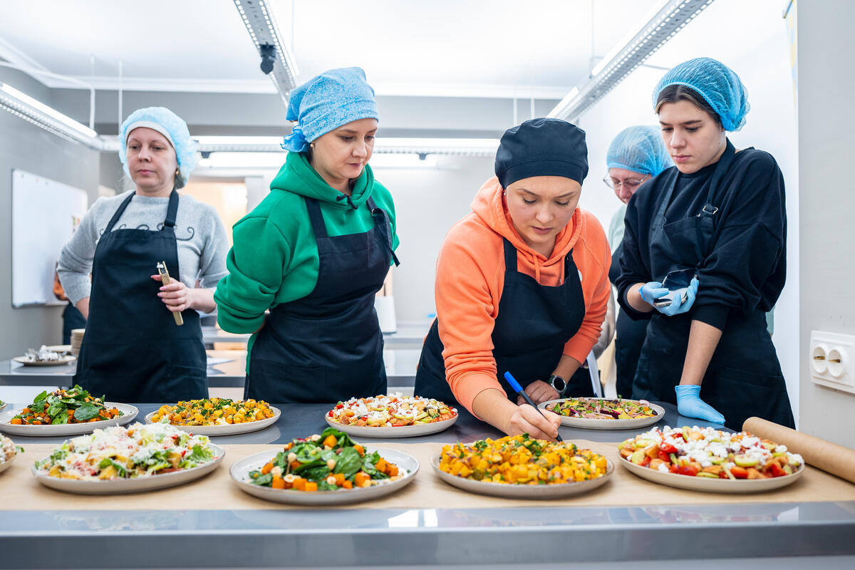 Ukrainian refugee women wear hairnets and overlooking the plates of food they cooked